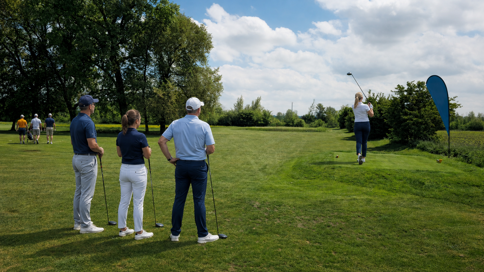 Golferin schlägt an Bahn 2 über den Teich, drei Flightpartner beobachten den Ball Richtung Green.
