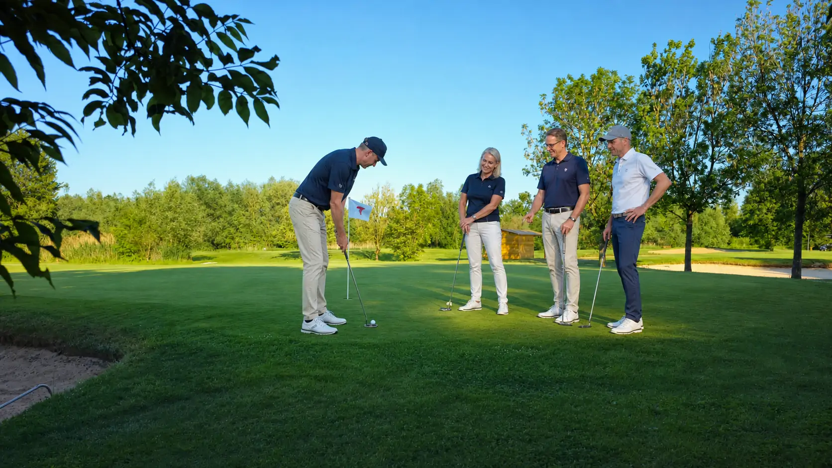 Vier Unternehmensvertreter auf dem Putting Green, ein Golfer bereitet einen Putt vor.
